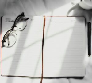 Blank open notebook with lined pages, with a pair of glasses resting on one page. 