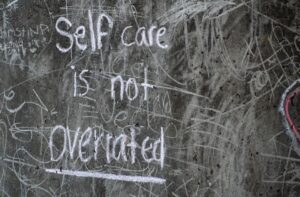 Image shows a blackboard with chalk writing reading ‘self care is not overrated’ mindful journaling