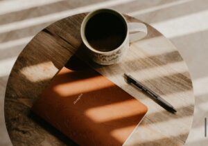 What to write in a journal. Image shows a closed journal on a coffee table next to a hot drink