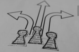 Image shows three ‘people’ silhouettes cut out from printed paper, positioned at the base of three arrows drawn in black marker pen, pointing in different directions 