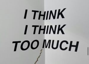 Image shows black writing on the corner of a wall reading ‘I think I think too much’ 