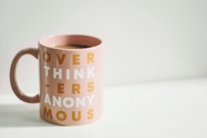 Why journaling helps with overthinking. Image shows a pale pink mug with ‘overthinkers anonymous’ written on it in yellow and white 