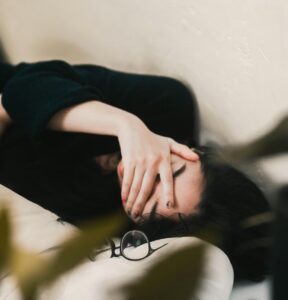 Decision fatigue. Image shows a woman laying down next to a pair of spectacles, with her hand over her face.