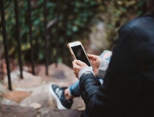 Image shows someone sat at the top of stone steps outdoors looking at a mobile phone 