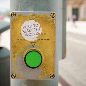 Weekly reset routine. Image shows a pedestrian crossing button with a sticker on it reading ‘push to reset the world’