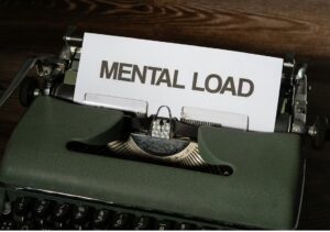 Brain feels too full. Image shows a typewriter with paper showing typed text reading ‘mental load’ in large capital letters