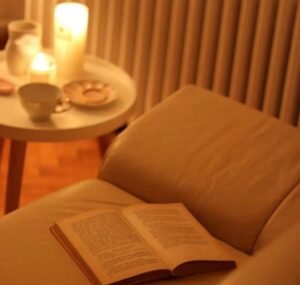 Image shows an open book on a sofa, next to a small table with lit candles on it