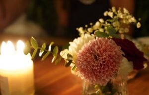 Image shows a closeup of a candle and vase of flowers on a table